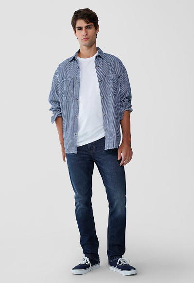 A male model wearing slim jeans and a striped button-down shirt.