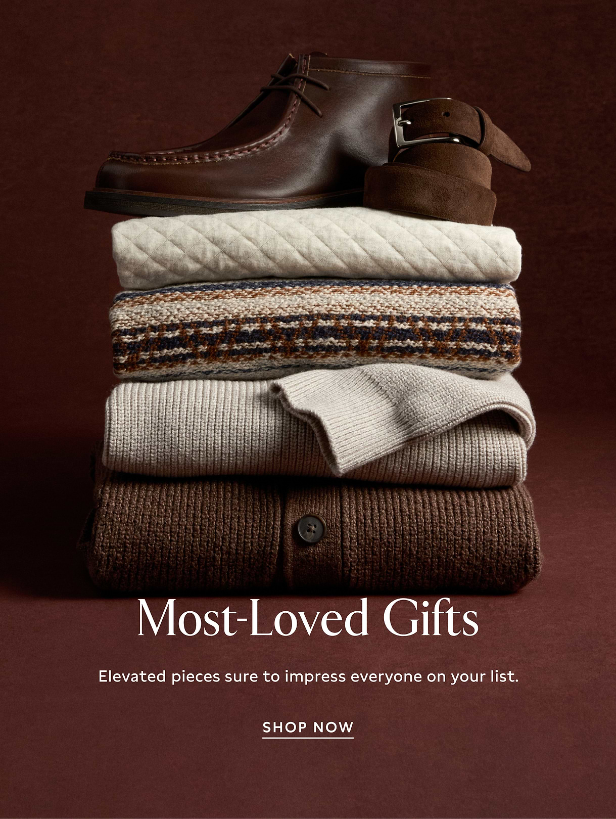 Alt text: Stack of folded neutral-toned sweaters with brown leather boots and a suede belt on top; brown background with text reading “Most-Loved Gifts” and “Shop Now.”