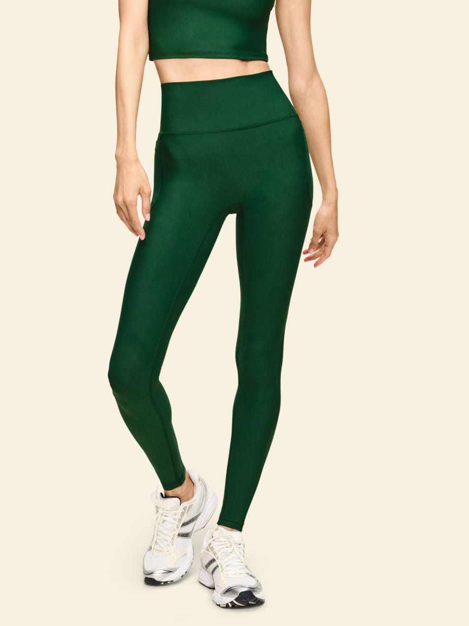High-waisted dark green leggings on a person, paired with white running shoes.
