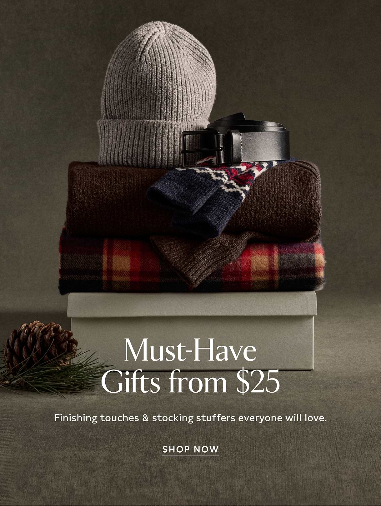 Stacked winter accessories—a gray knit beanie, black belt, patterned socks, and folded sweaters—on a gift box with text: “Must‑Have Gifts from $25” and “Shop Now.”