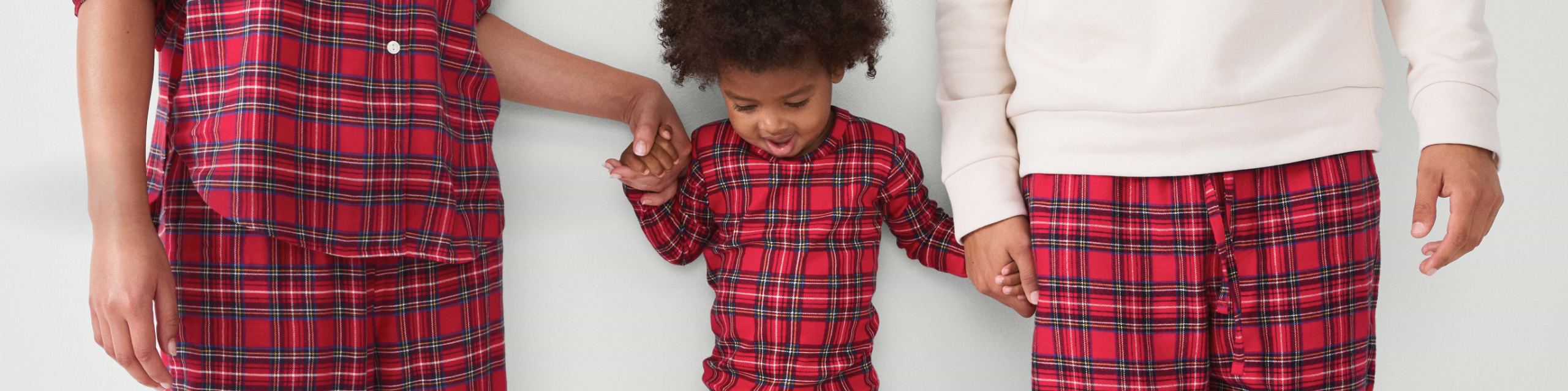 Child in red plaid pajamas holding hands between two adults wearing matching red plaid pajamas.