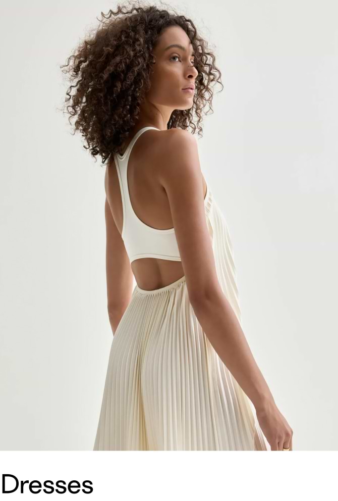Back view of a woman in an ivory pleated dress with a racerback and waist cutout.
