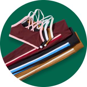 Stack of colorful sports bras and matching leggings with contrasting straps and side stripes on a green background.