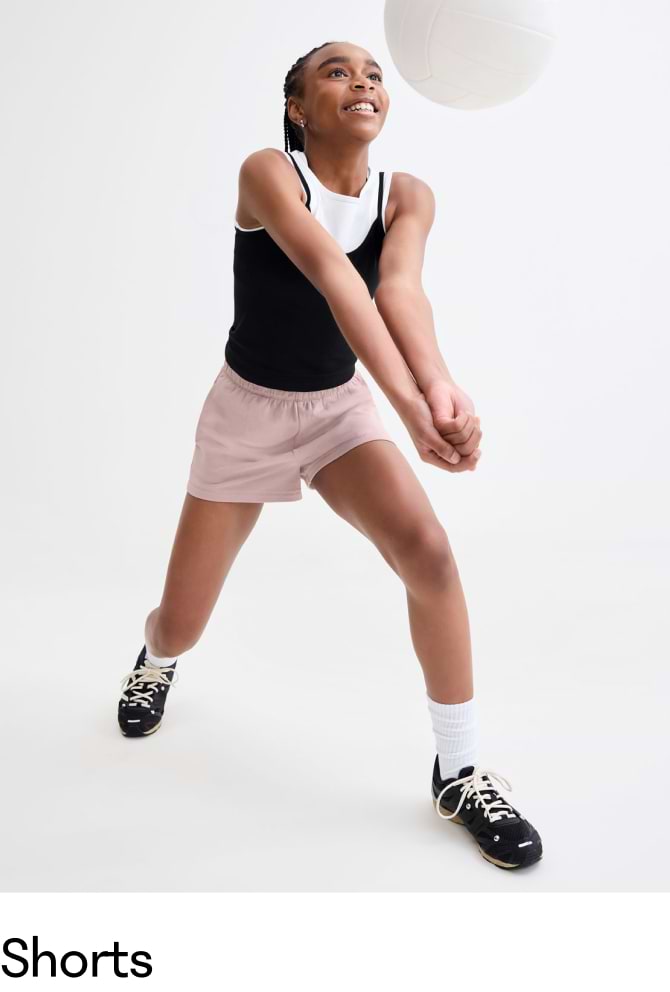 Girl in pink athletic shorts and black top bumping a volleyball.