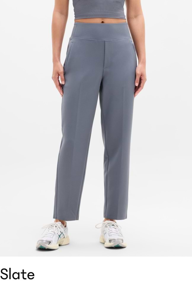 Model wearing slate gray high‑waisted, straight‑leg ankle pants with side pockets and front seam, paired with white sneakers.