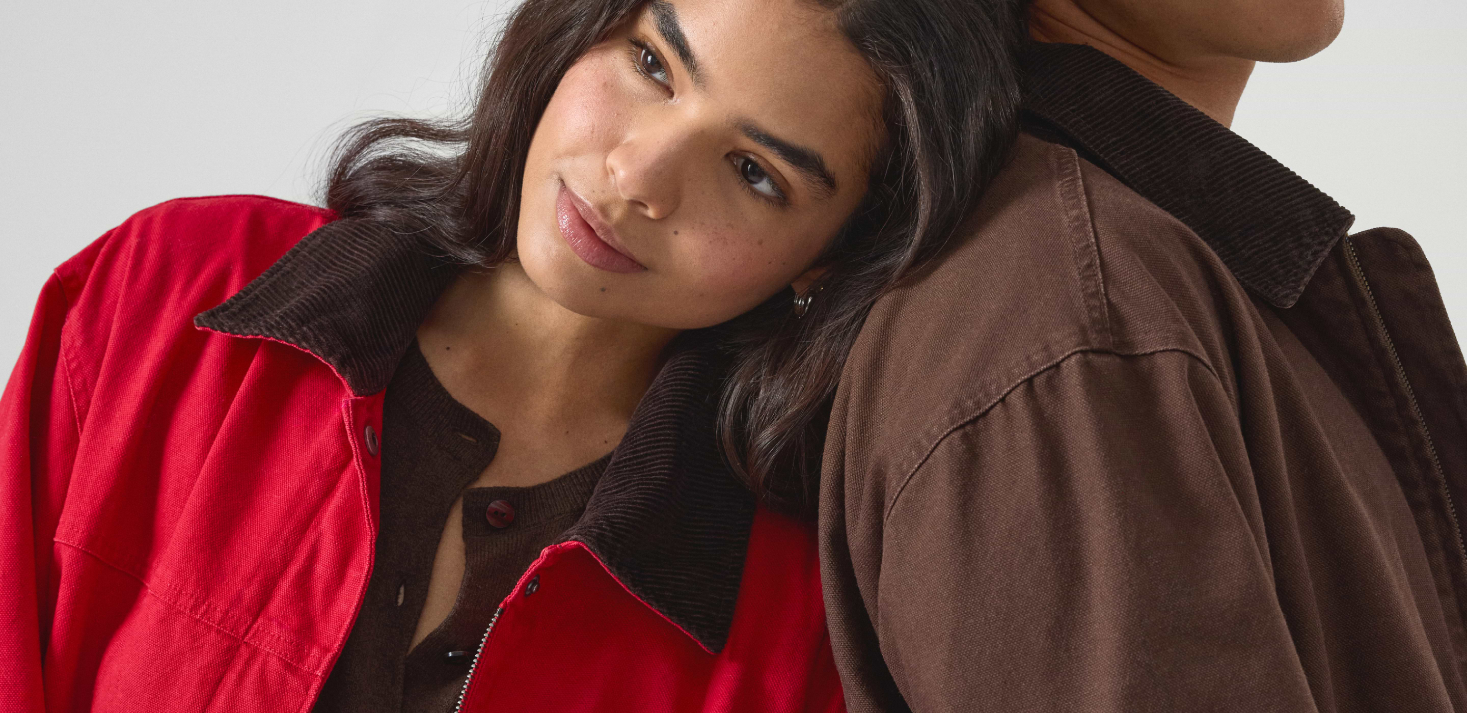 Close-up of a person in a red jacket with a brown corduroy collar, resting their head on another person wearing a brown jacket.