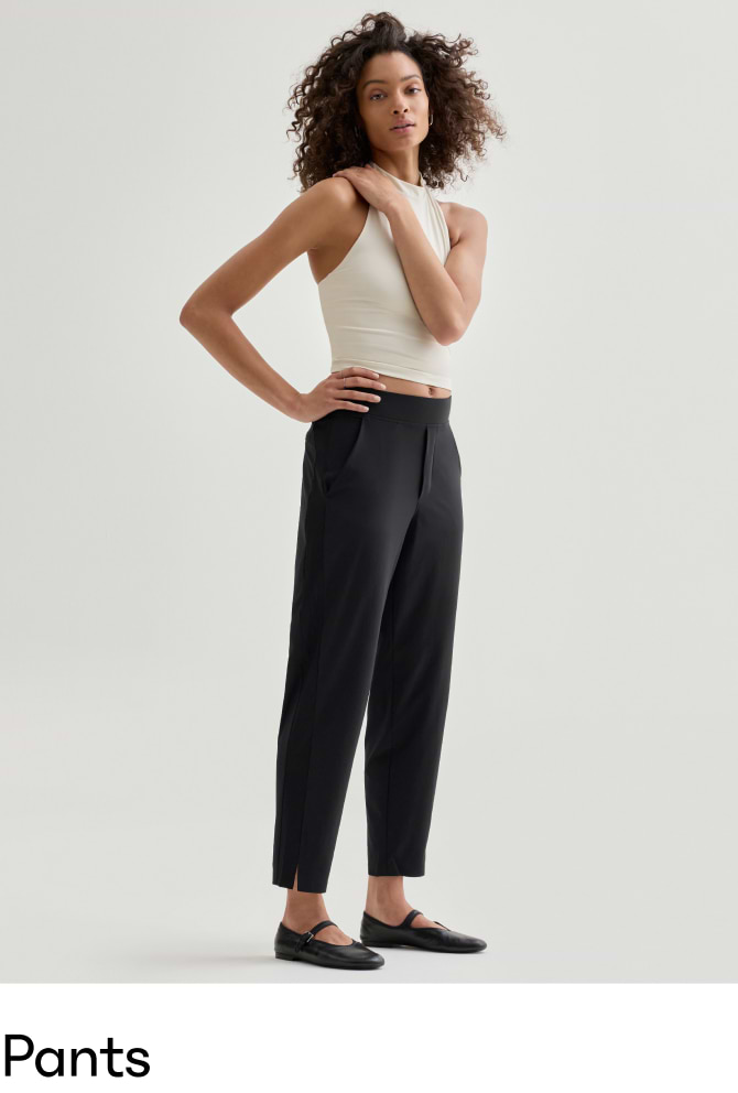 Woman modeling black tailored ankle‑length pants with pockets, paired with a white sleeveless crop top and black flats.