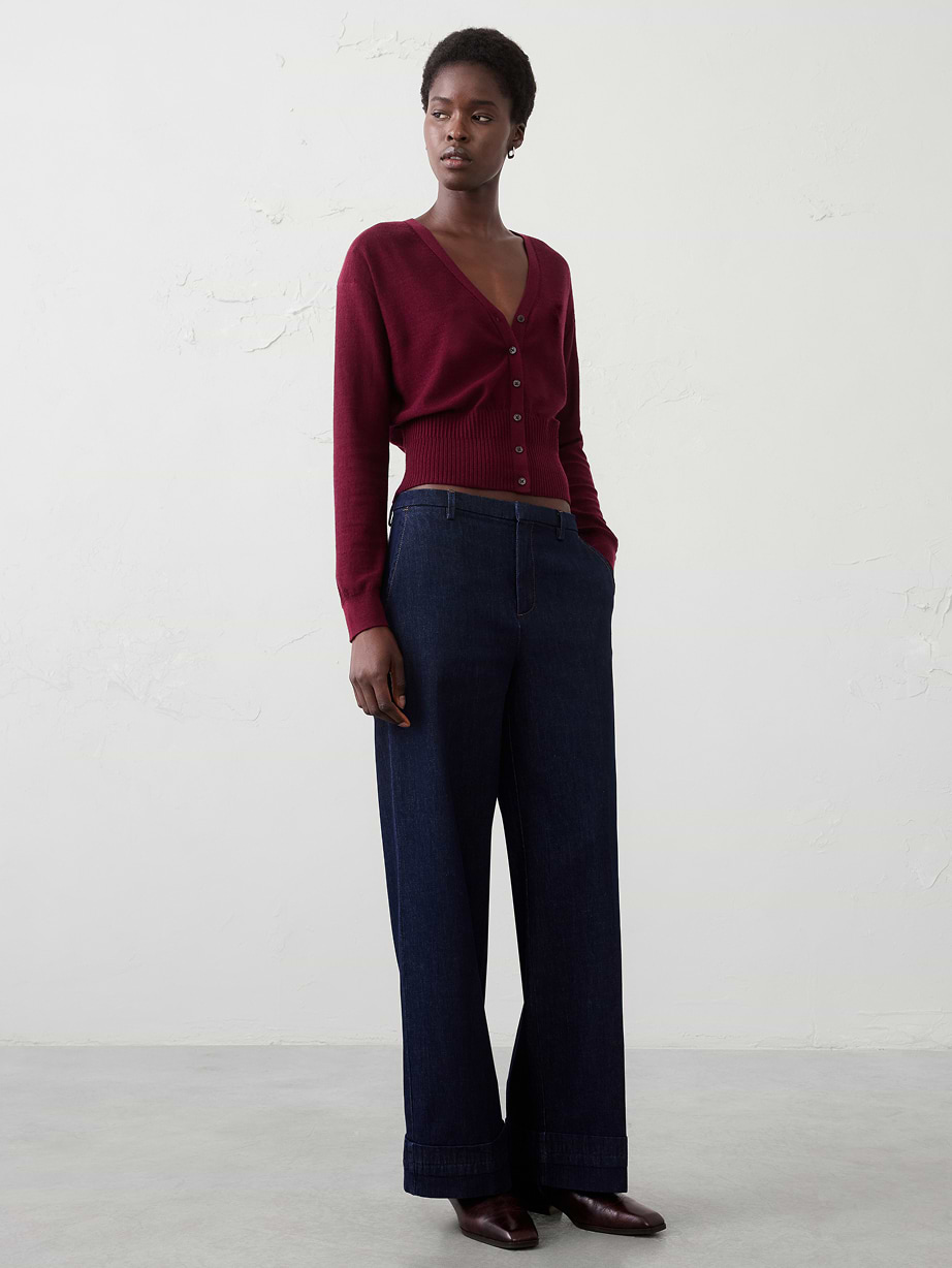 Person wearing a burgundy V‑neck cardigan and dark wide‑leg cuffed jeans, standing with hands in pockets.