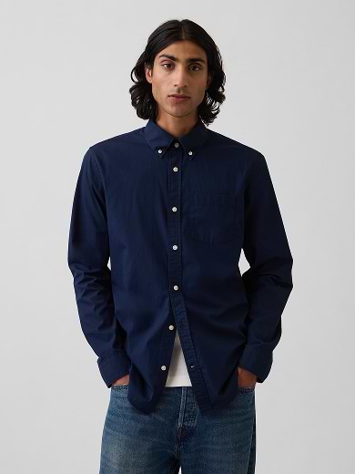 Person wearing a navy button-down shirt over a white tee and jeans, standing against a plain background.