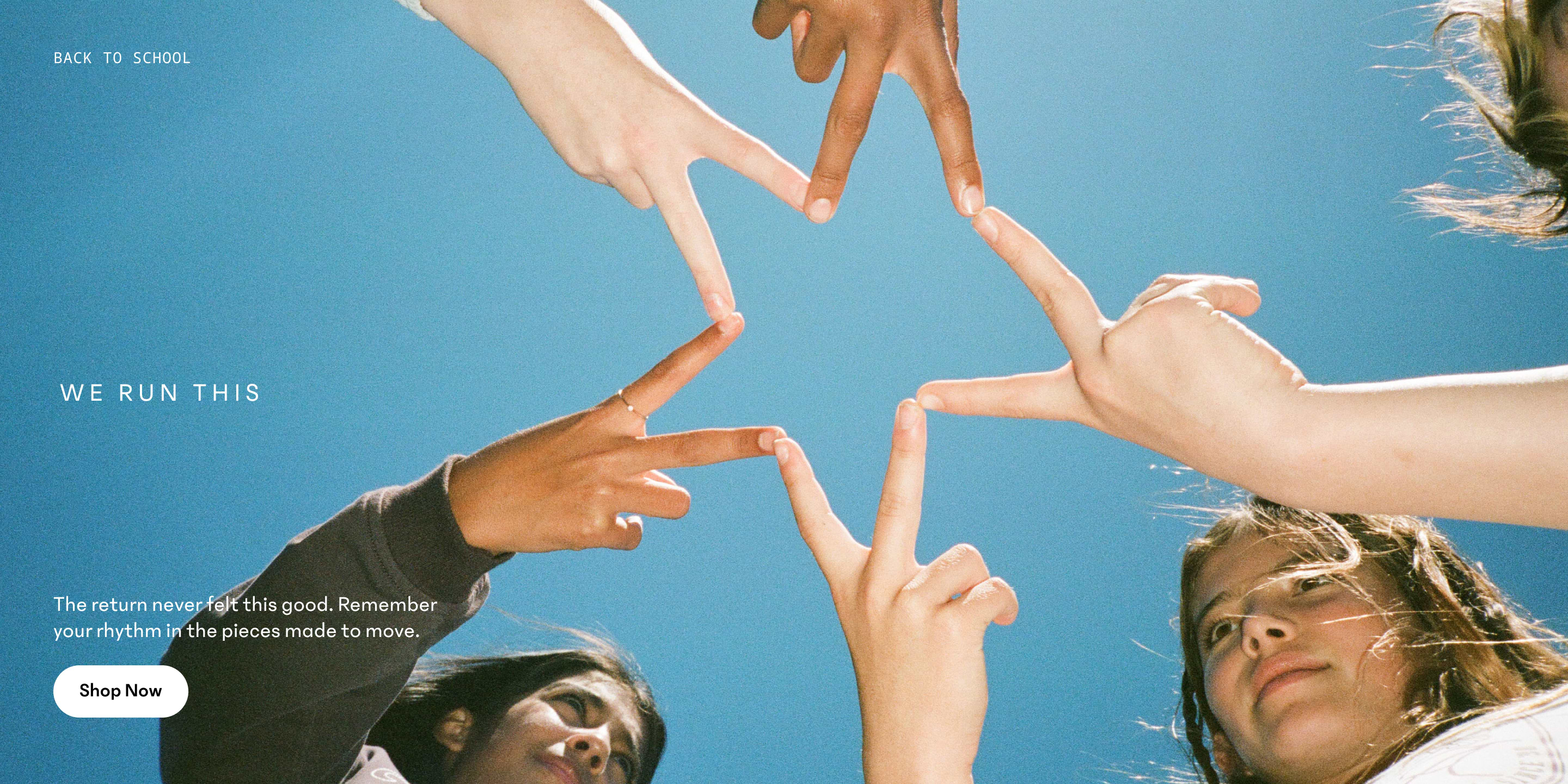Five girls join their fingers to form a star, seen from below against a clear blue sky.