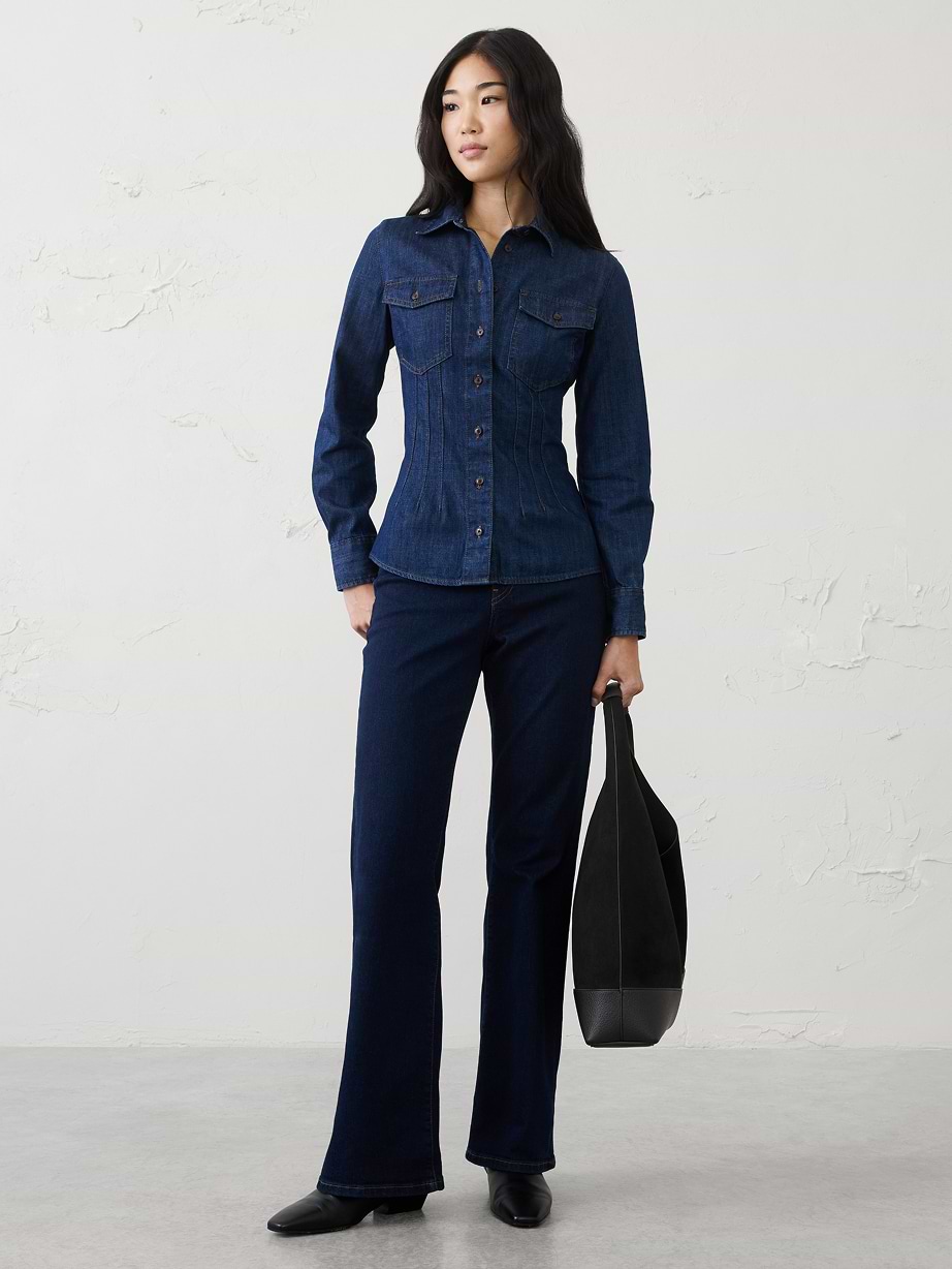 Person in dark denim shirt and flared jeans holding a black tote bag.